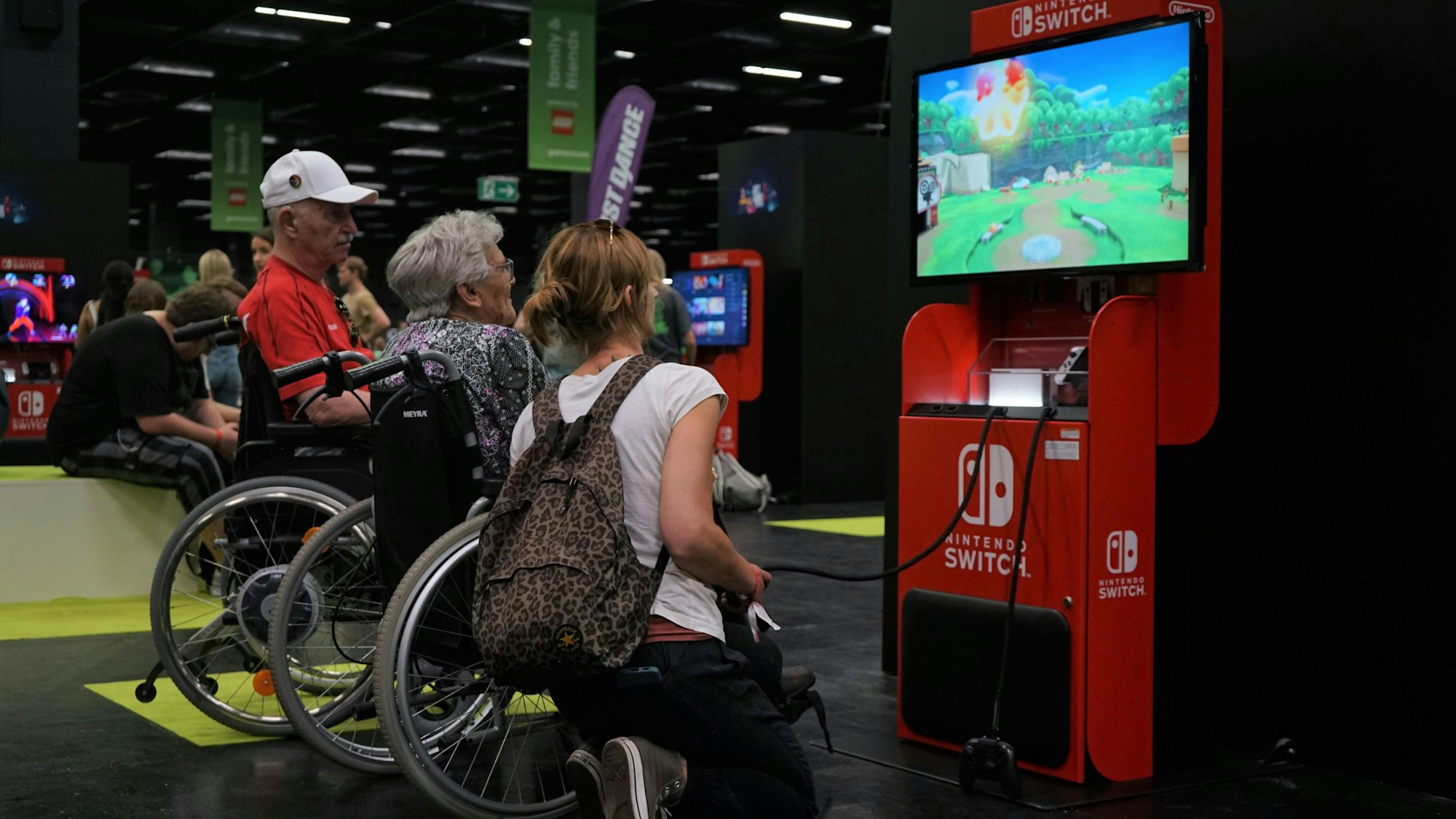 Zwei Senioren und eine Pflegekraft spielen ein Videospiel auf der Nintendo Switch auf der Gamescom.