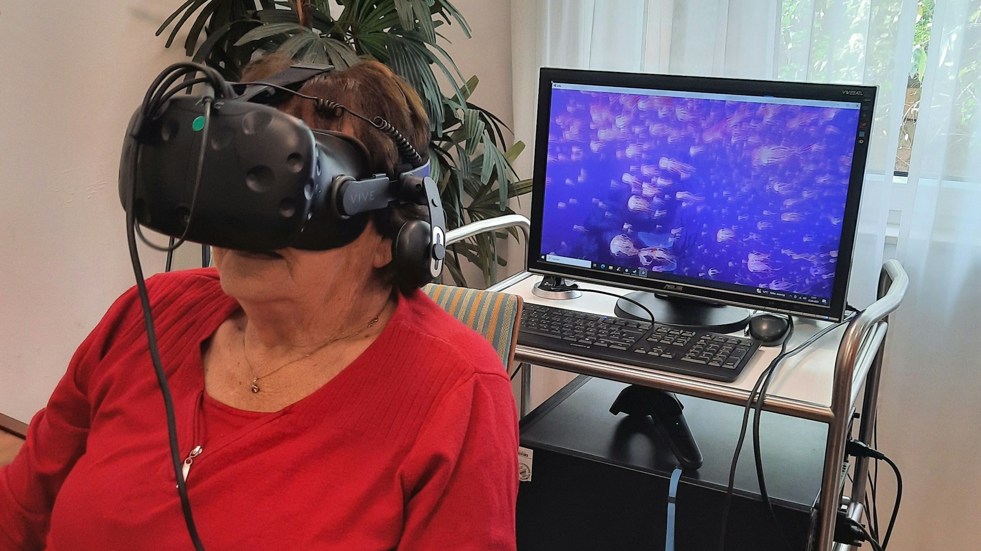 Eine Bewohnerin des Caritas-Altenzentrums hat eine VR-Brille auf und blickt in eine Unterwasserwelt mit Quallen.