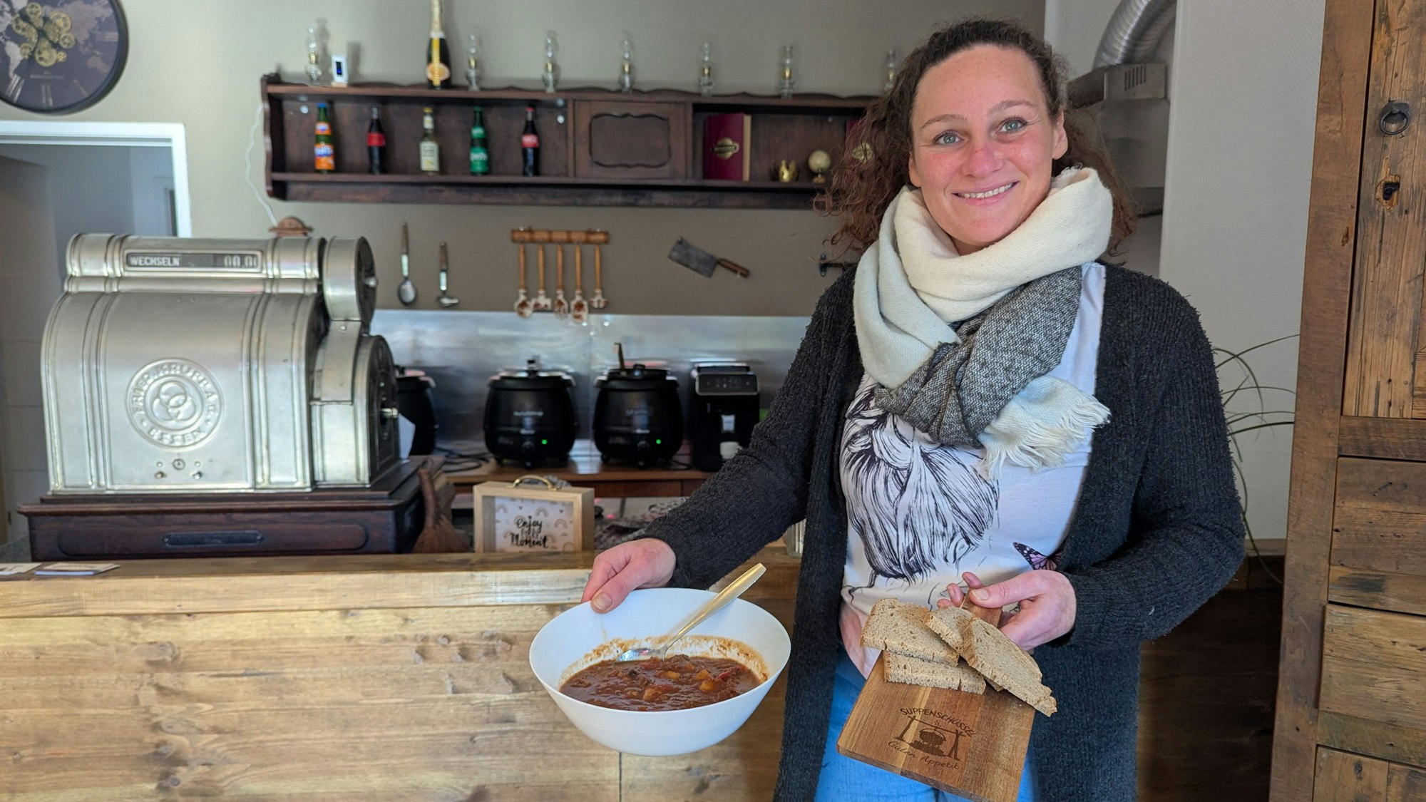 Das Foto zeigt die Inhaberin mit einer Terrine Suppe und Brot vor der Theke der Gaststätte.