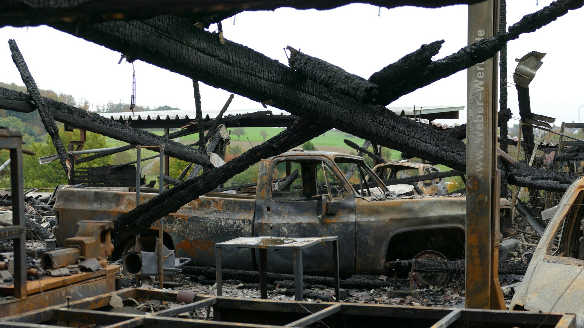 Ausgebrannte Autos stehen in der zerstörten Halle. Schwarz verkohlte Balken hängen schief herum.