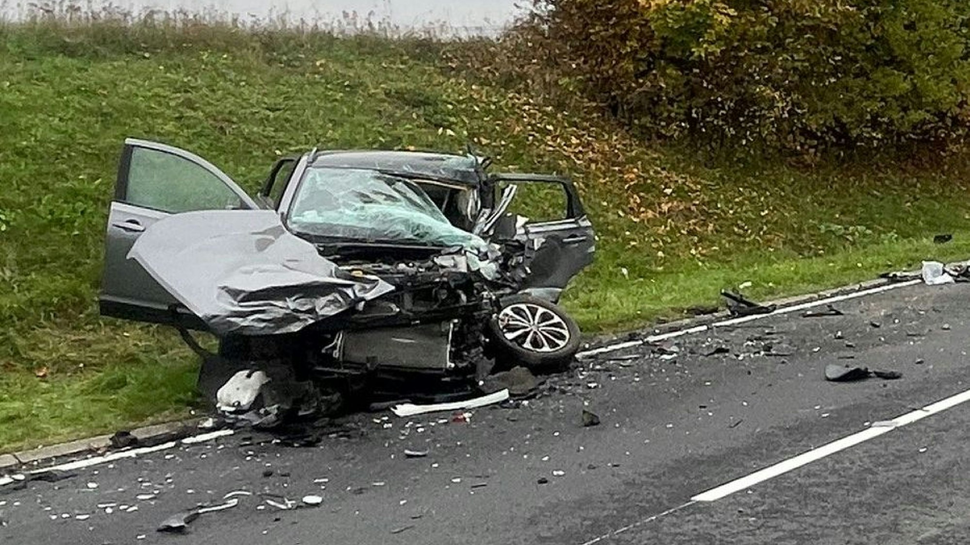 Ein zerstörtes Auto ist neben einer Straße zu sehen.