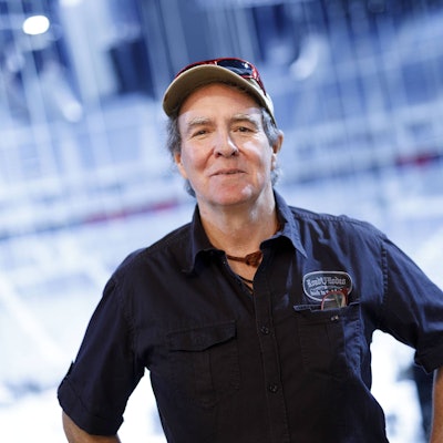 Sänger Peter Horn lächelt mit Kappe, Hemd und „Roadie Rodeo“ Patch vor blauem Hintergrund.