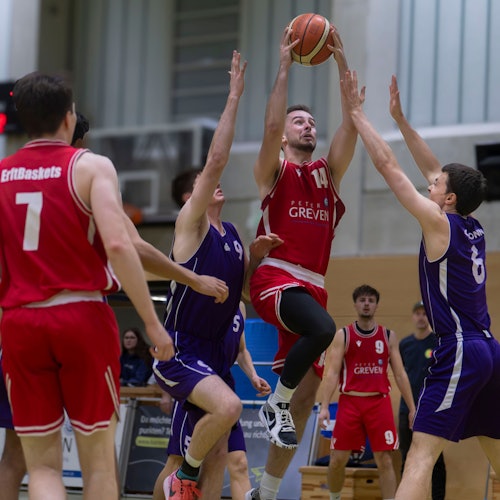 Erftbaskets-Spieler Chris Beier steigt zum Korb hoch und kann auch von zwei Gegenspielern, die die Arme hochreißen, nicht aufgehalten werden.