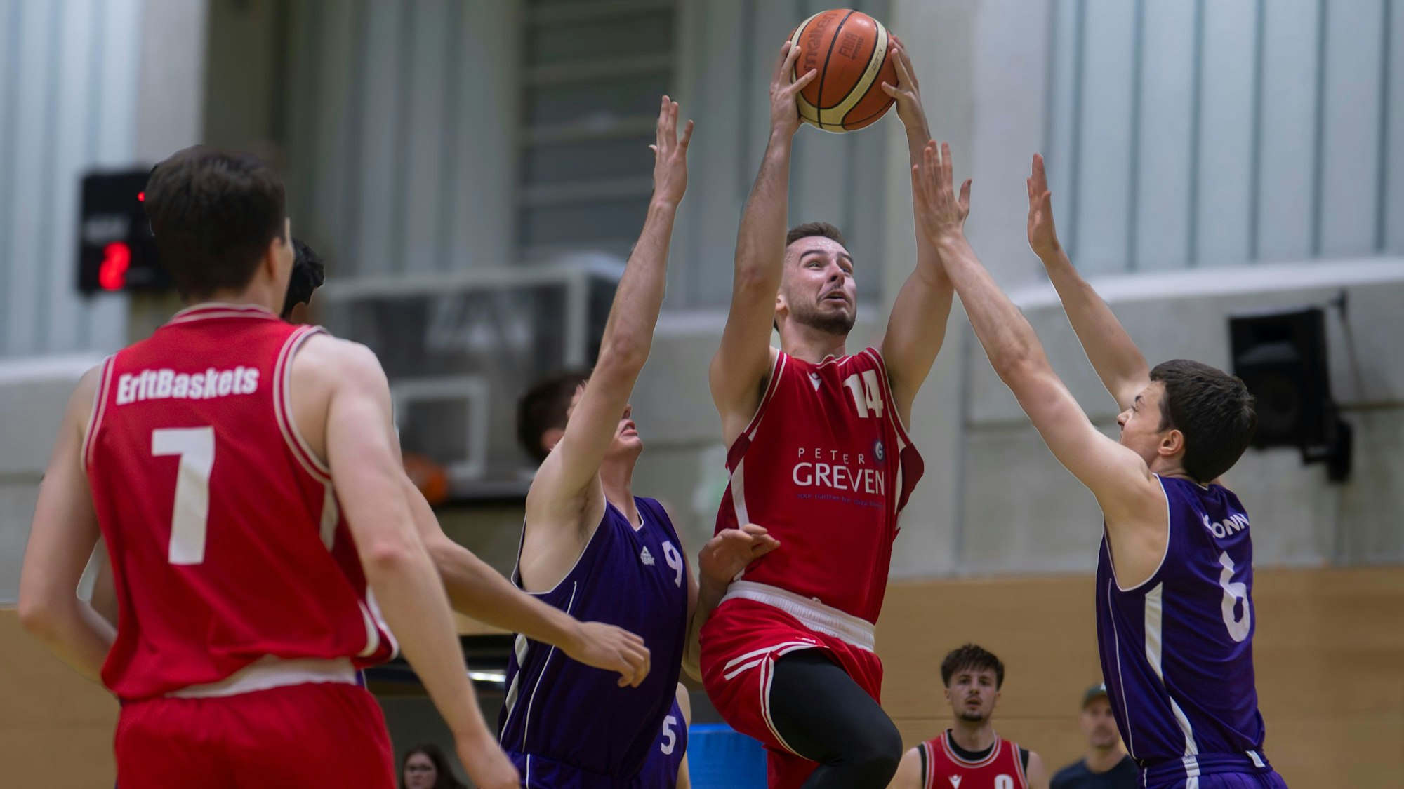 Erftbaskets-Spieler Chris Beier steigt zum Korb hoch und kann auch von zwei Gegenspielern, die die Arme hochreißen, nicht aufgehalten werden.