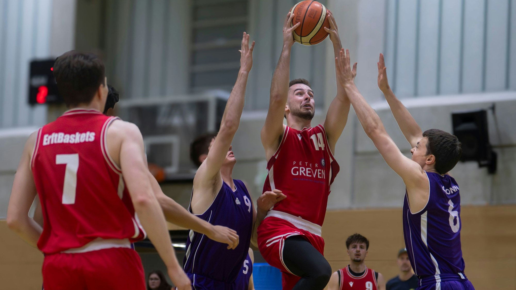 Das Bild zeigt einen Basketballer, wie er gegen zwei Gegenspieler zum Korb zieht.