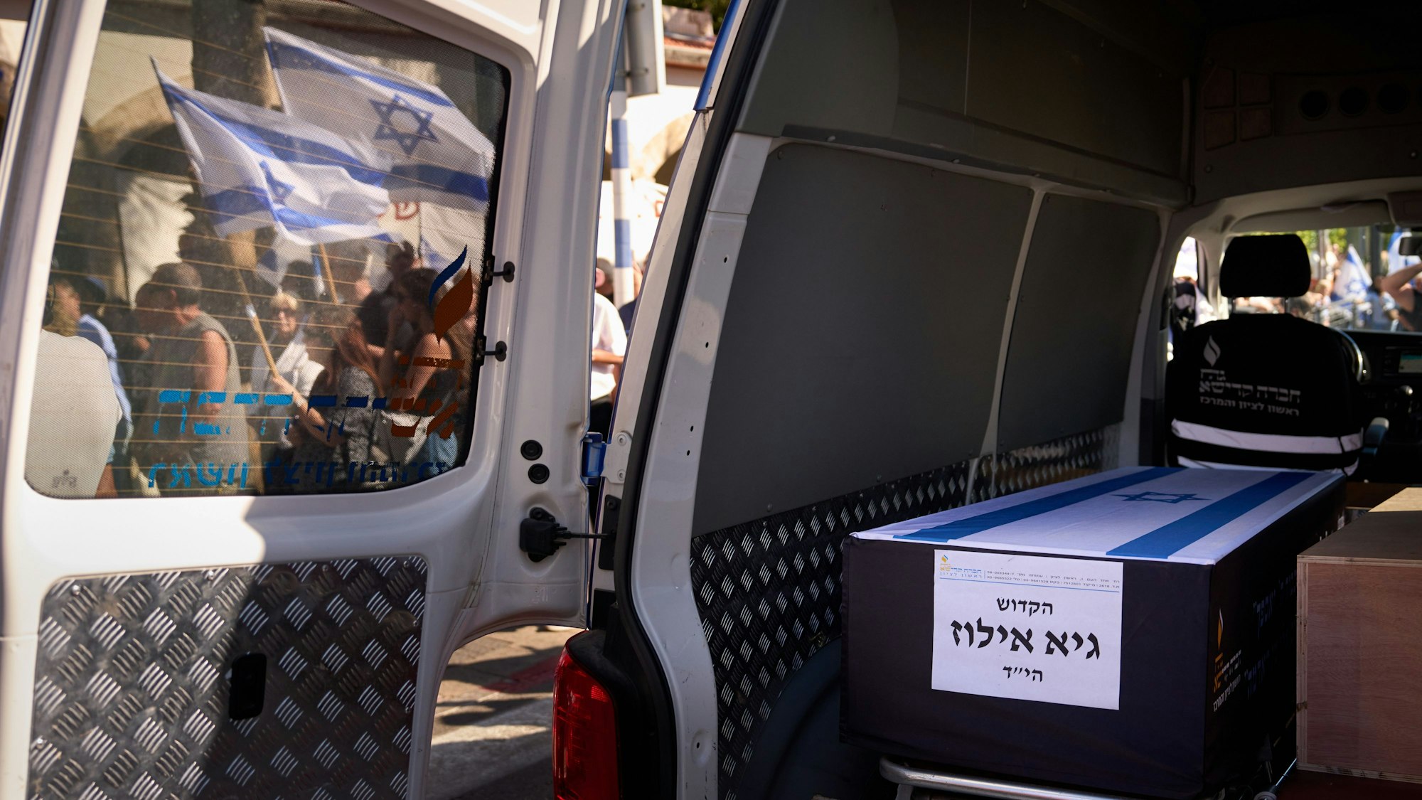 Das Bild zeigt Trauernde die sich in der Nähe des Wagens, in dem der Sarg der getöteten Geisel Guy Illouz transportiert wird, während eines Trauerzuges versammeln. Foto: Emilio Morenatti/AP/dpa