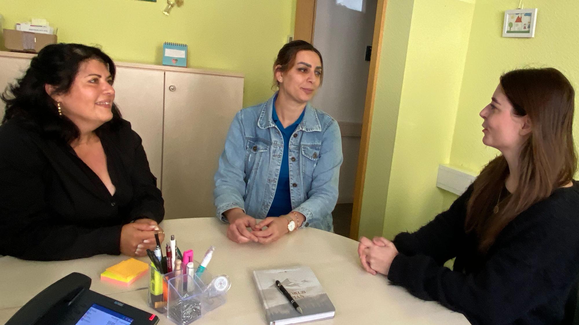 Drei Frauen sitzen an einem Tisch und unterhalten sich.
