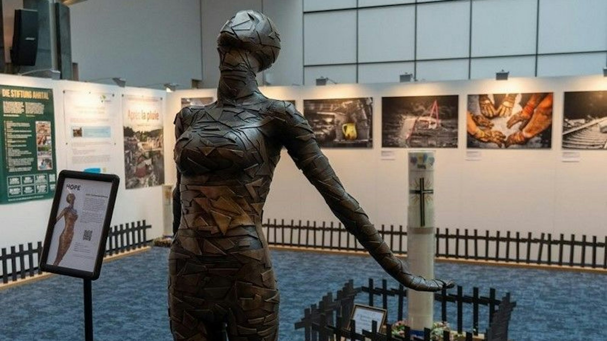 Die Bronzeskulptur „Hope“ von Dennis Josef Meseg zwischen Gemälden, Plakaten, Fotos und einem Saum aus schwarzen Kreuzen für jedes Opfer