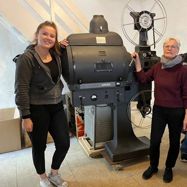 Das Foto zeigt zwei Frauen und einen Mann vor dem historischen Filmprojektor.