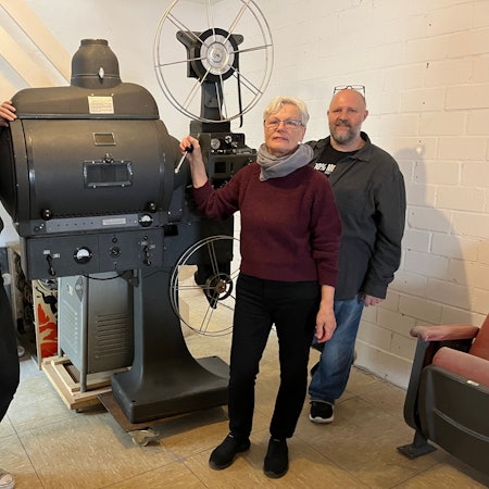 Das Foto zeigt zwei Frauen und einen Mann vor dem historischen Filmprojektor.
