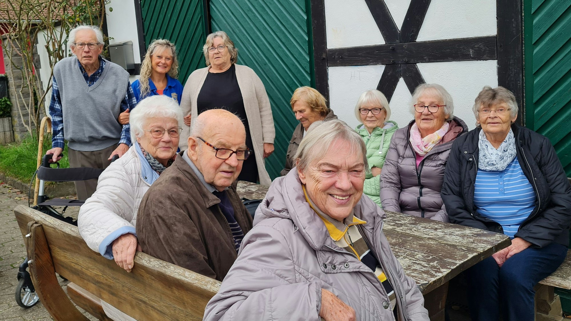 Eine Gruppe von Senioren sitzt vor einem Fachwerkhaus.