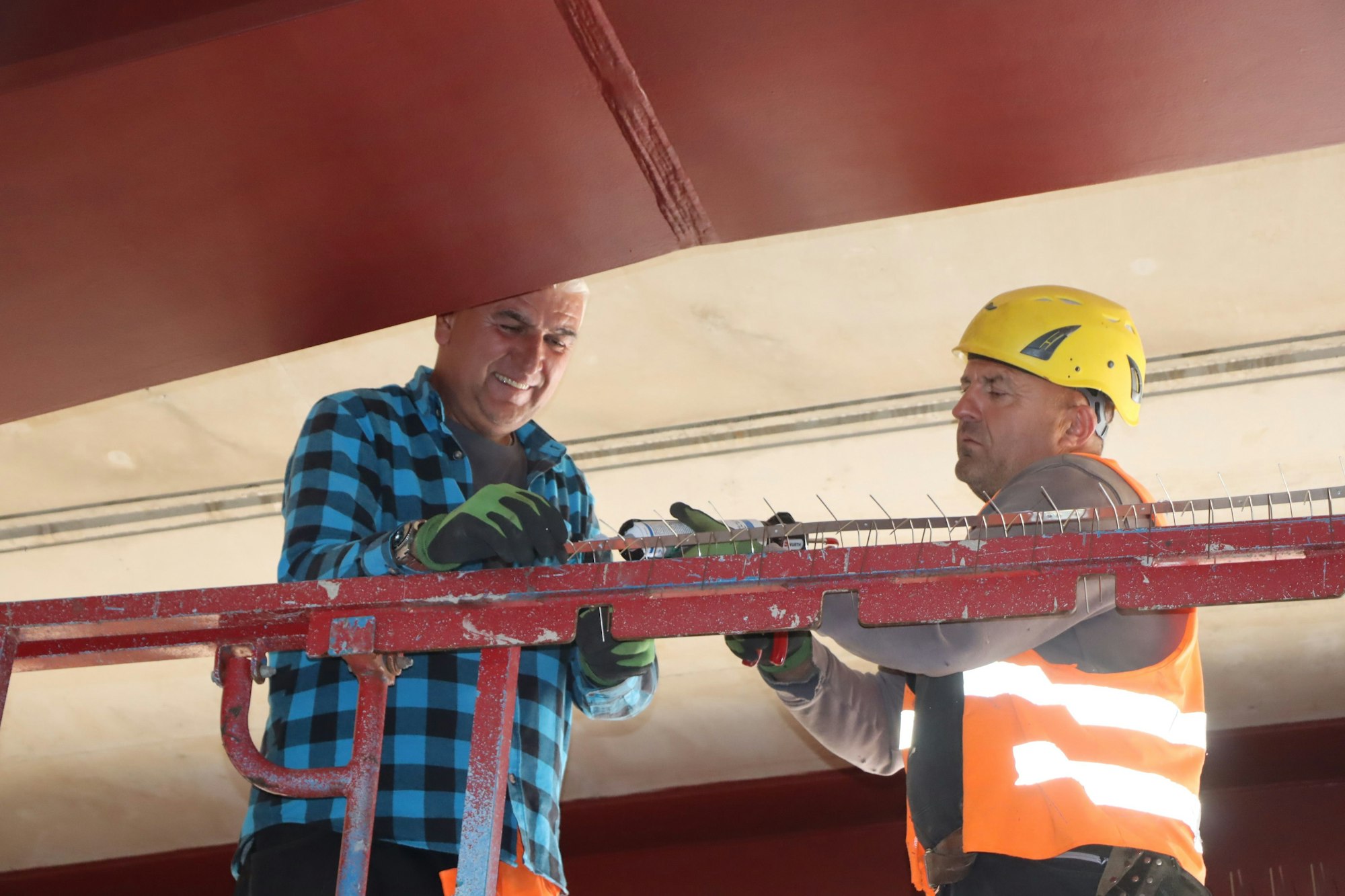 Das Bild zeigt zwei Herren beim Anbringen der Spikes. Sie tragen Handschuhe, einer trägt einen gelben Helm und eine Warnweste.