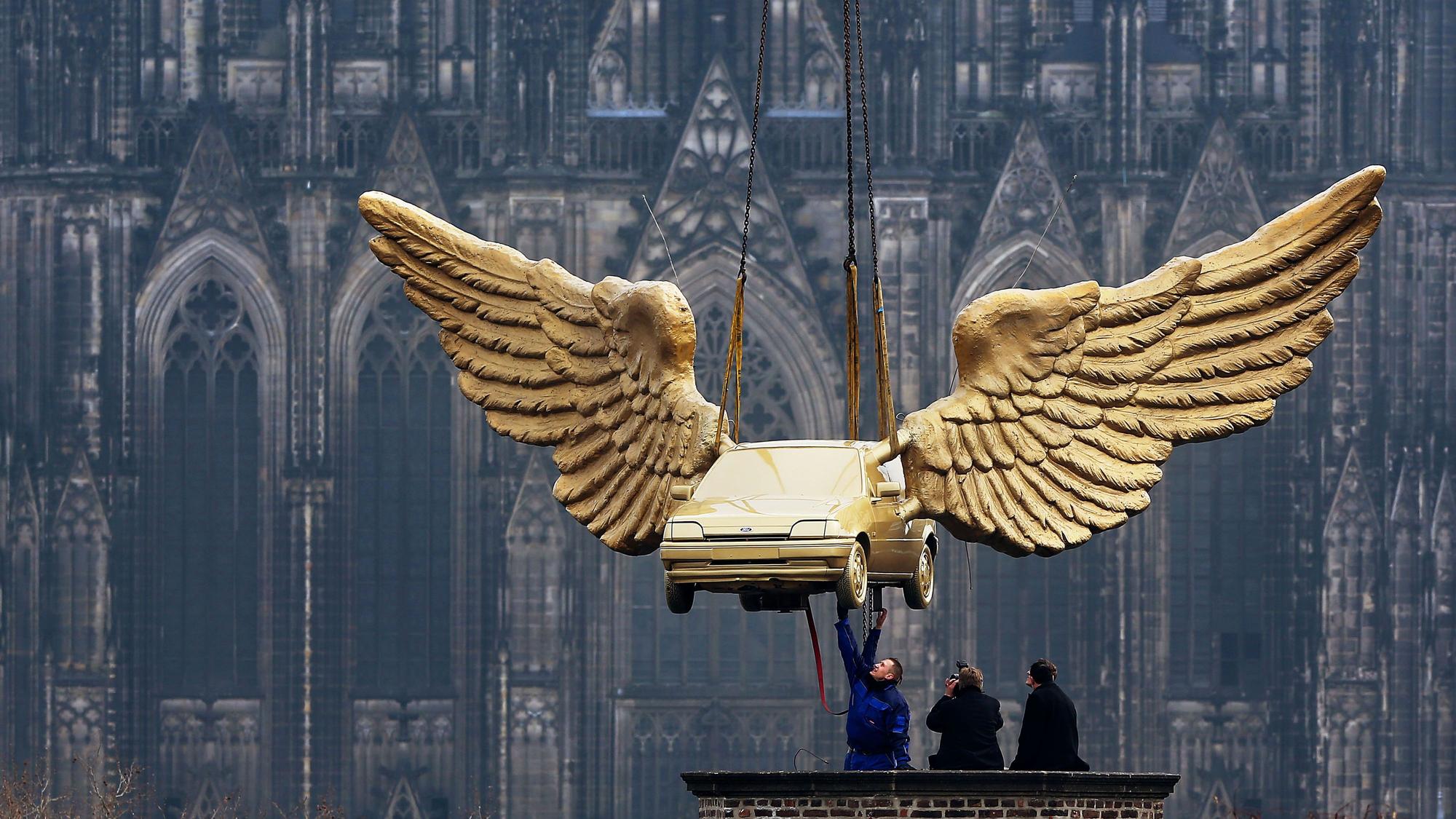 Köln: Arbeiter nehmen auf dem Dach des Kölnischen Stadtmuseums das Flügelauto des Künstlers HA Schult entgegen.