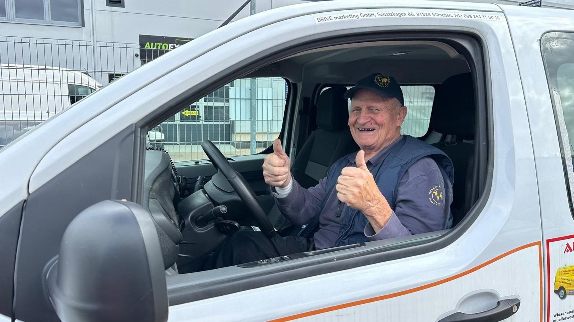 Norbert Kuhl sitzt mit nach oben gestreckten Daumen am Steuer eines mit Werbung beklebten Opel-Kastenwagens.