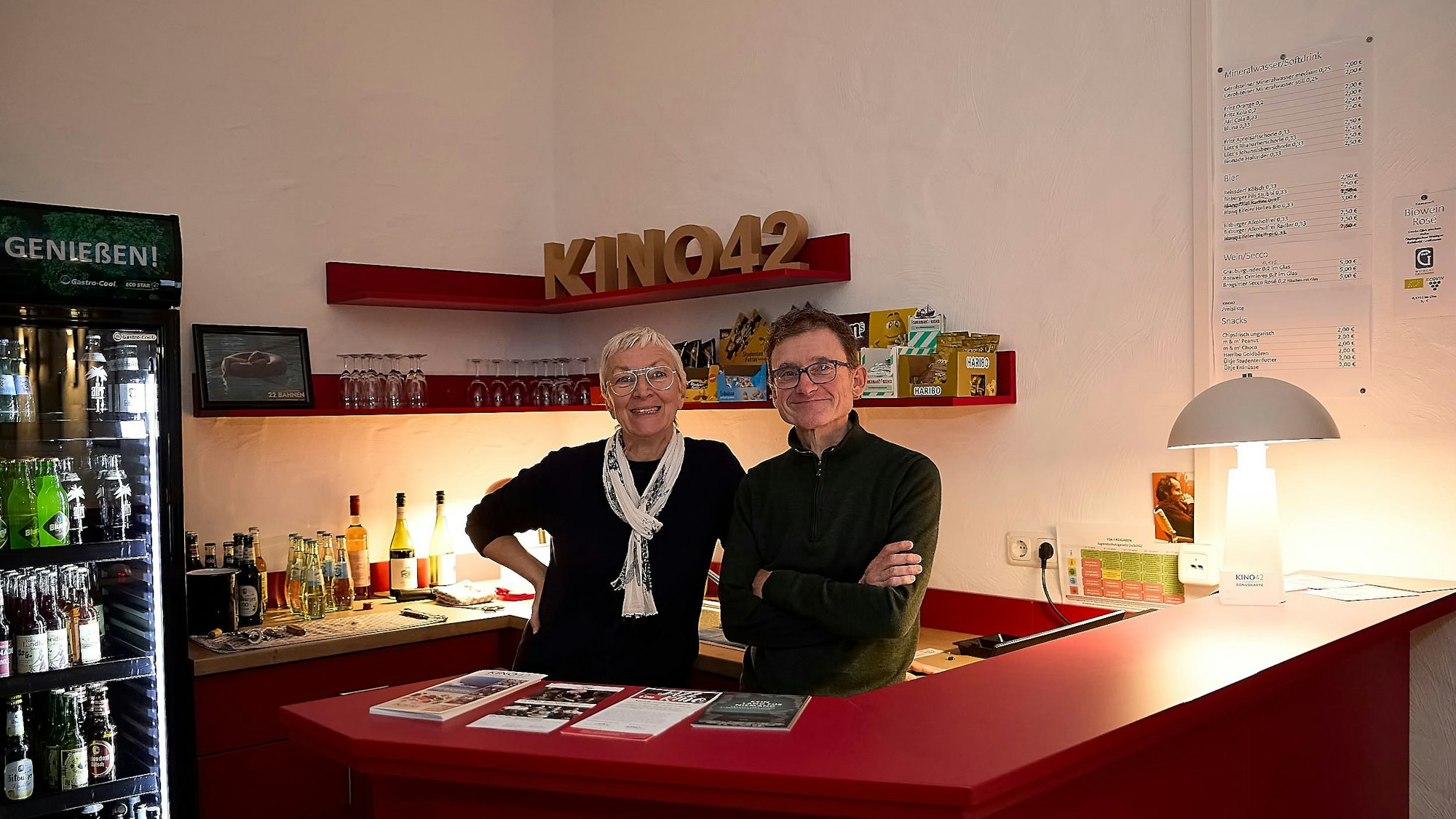 Eine Frau und ein Mann stehen hinter einem Tresen, im Hintergrund Flaschen und Gläser.