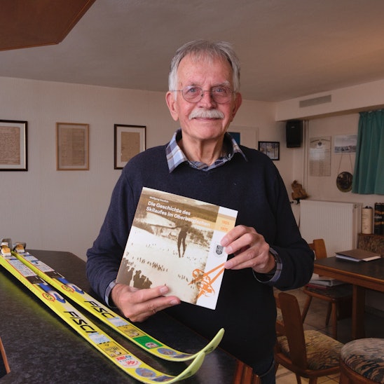 Wolfgang Gaudich hält sein Buch über den Skisport im Oberbergischer Kreis in den Händen. Auf dem Tisch im Hintergrund liegen Langlaufski.