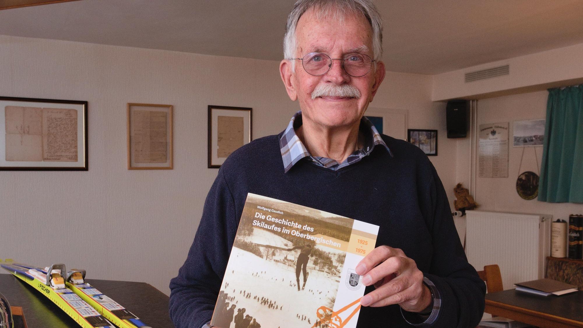 Wolfgang Gaudich hält sein Buch über den Skisport im Oberbergischer Kreis in den Händen. Auf dem Tisch im Hintergrund liegen Langlaufski.