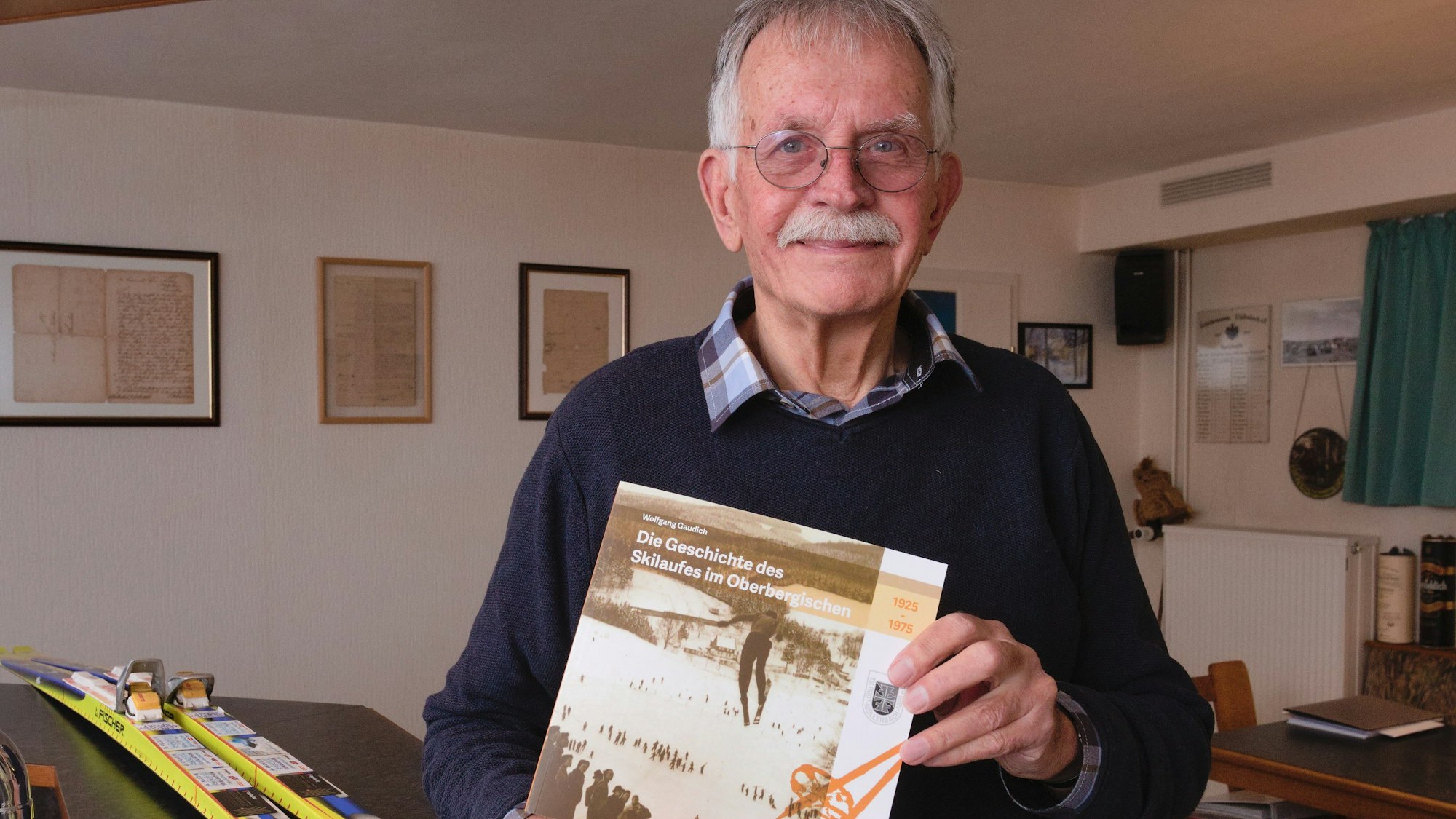 Wolfgang Gaudich hält sein Buch über den Skisport im Oberbergischer Kreis in den Händen. Auf dem Tisch im Hintergrund liegen Langlaufski.