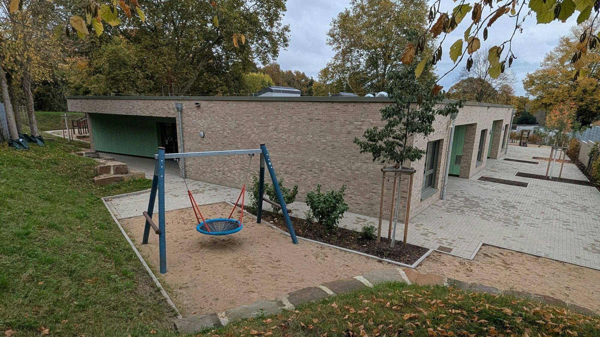 Das Foto zeigt eine Außenaufnahme der Kita und des Außenbereichs mit Nestschaukel.