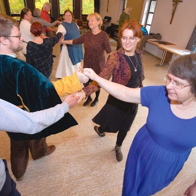 Frauen und Männer üben bei einem Tanzkurs Reigentänze aus vergangener Zeit.