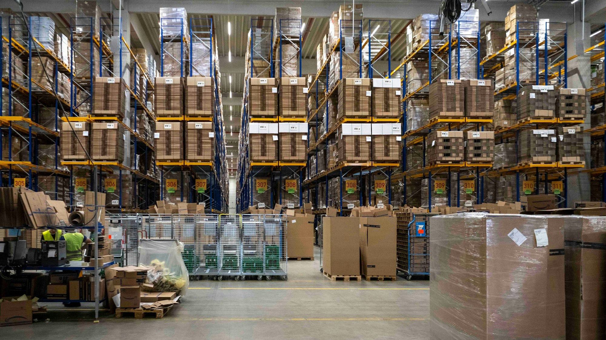 Das Bild zeigt hohe Regale, die mit Paletten und Kartons gefüllt sind.