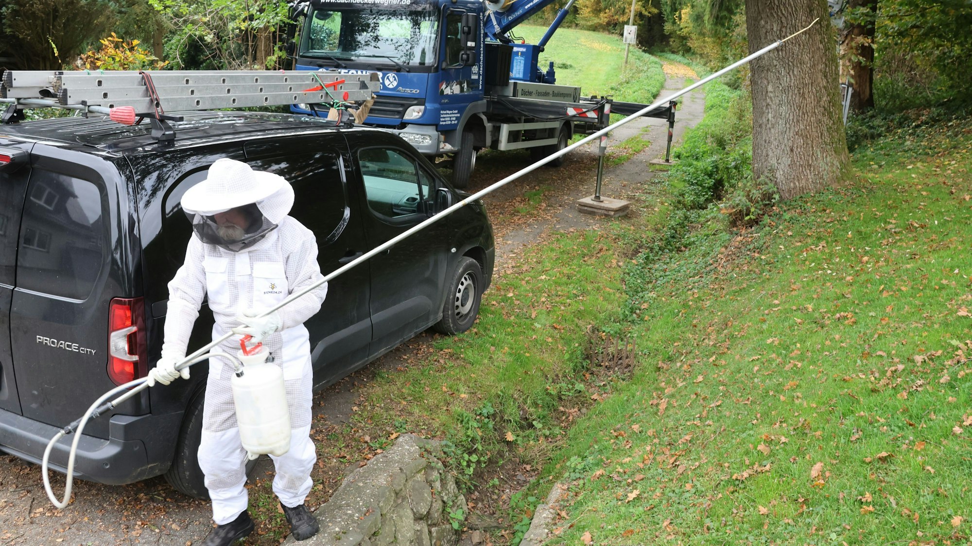 Ein Imker in Schutzanzug hält eine vier Meter lange Lanze mit einem Gift in den Händen.