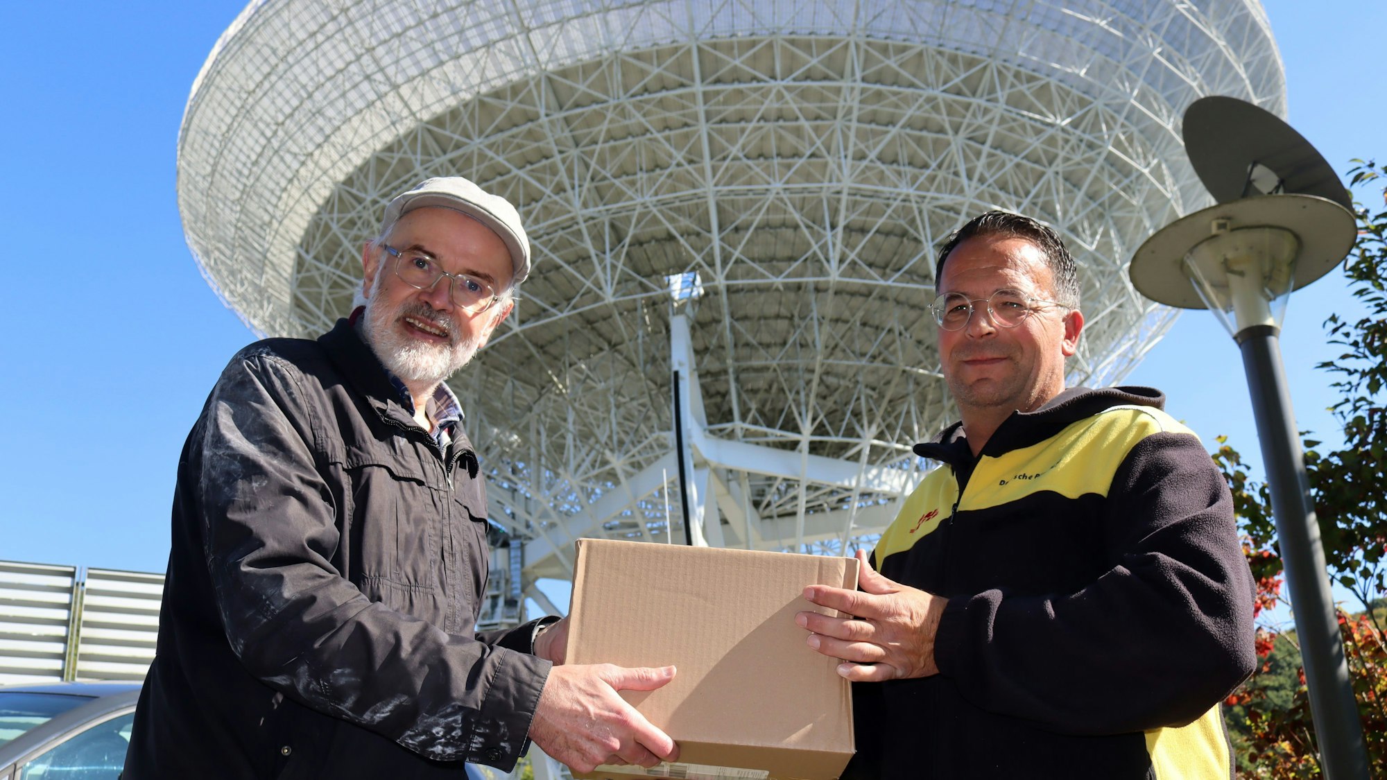 Das Bild zeigt die beiden Obengenannten, die gemeinsam ein Paket in den Händen halten.