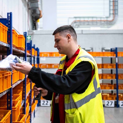 Das Bild zeigt den jungen Euskirchener, er an einem Regal steht und mithilfe eines Scanners Waren scannt.