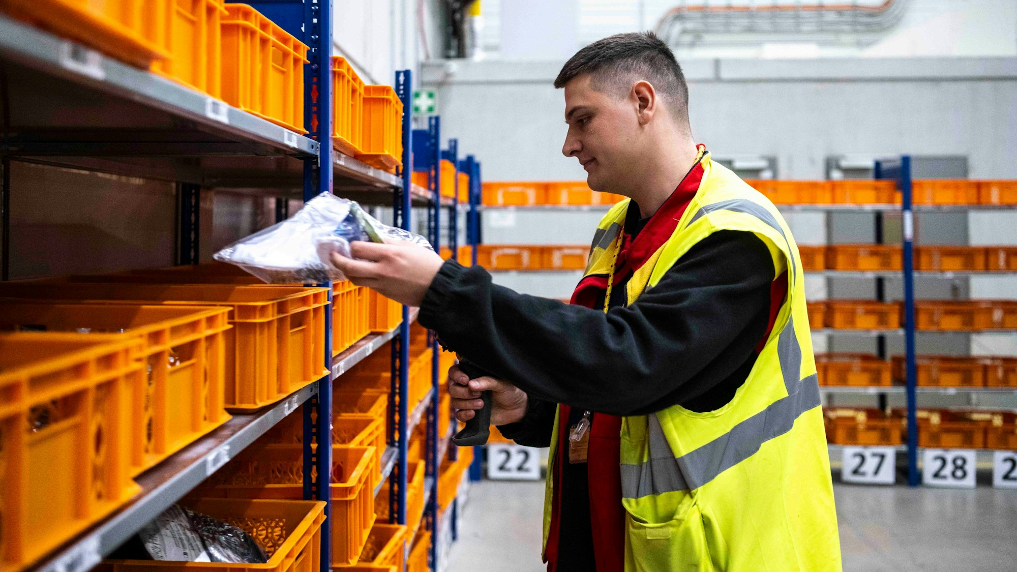 Das Bild zeigt den jungen Euskirchener, er an einem Regal steht und mithilfe eines Scanners Waren scannt.