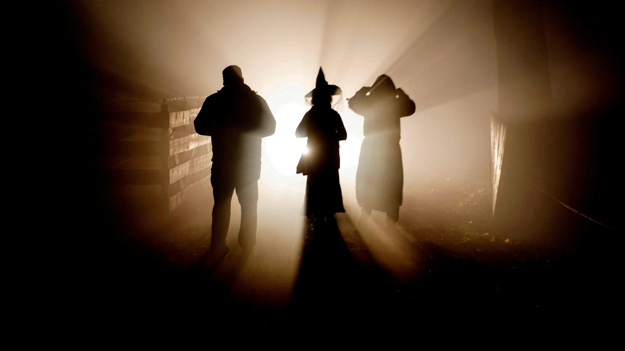 Drei Personen stehen im Gegenlicht, von ihnen sind nur die Umrisse zu erkennen.