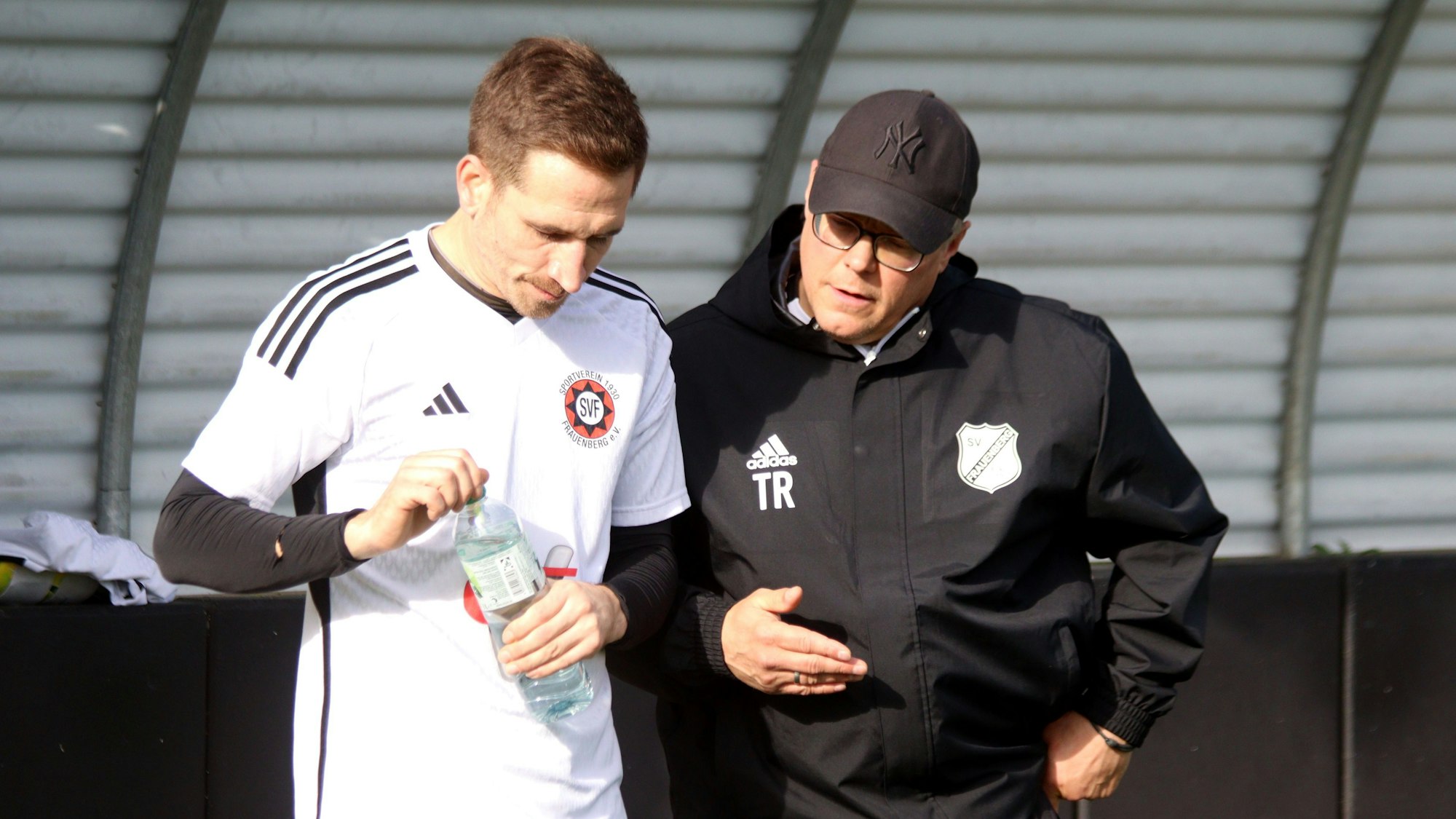 Marcel Timm steht neben seinem Spieler Marcel Motz und gibt ihm Anweisungen. Motz hält eine Flasche in den Händen.