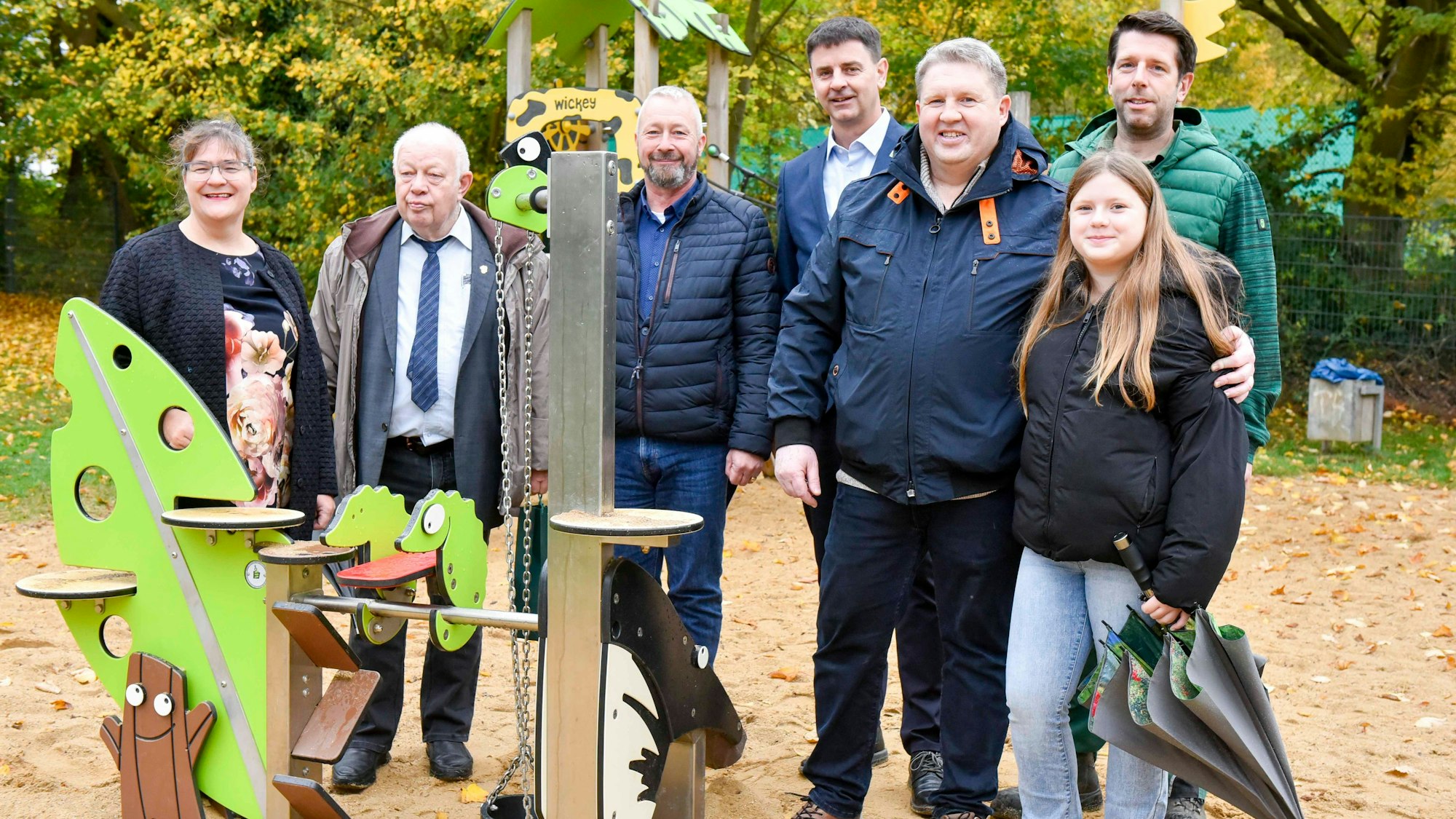 Männer und Frauen stehen nebeneinander auf einem Spielplatz vor Spielgeräten und lächeln.