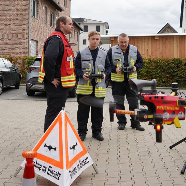 Das Foto zeigt drei Einsatzkräfte der Feuerwehr beim Fliegen einer Drohne.