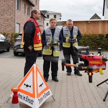 Das Foto zeigt drei Einsatzkräfte der Feuerwehr beim Fliegen einer Drohne.