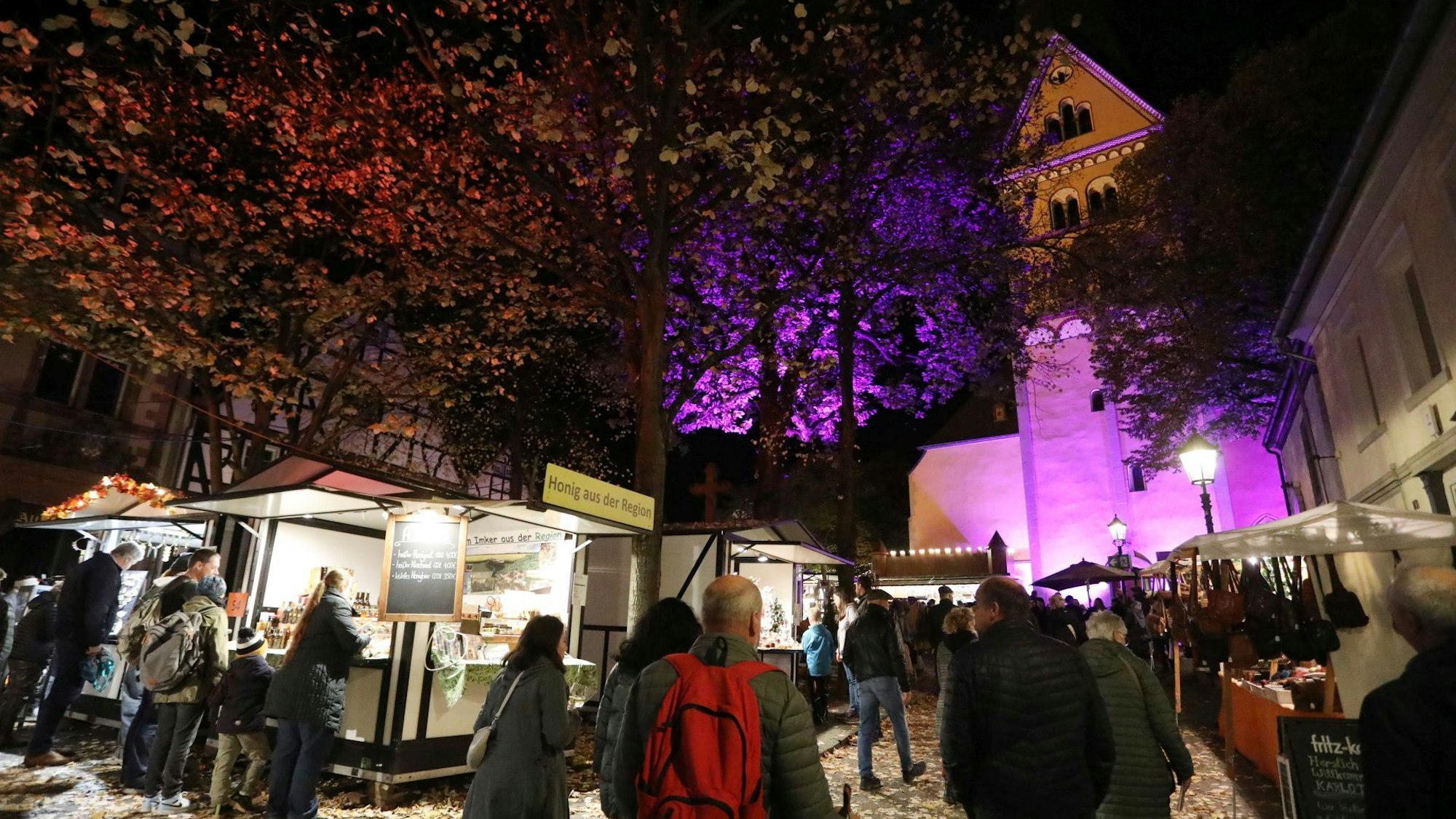 Menschen an mehreren Marktbuden, im Hintergrund eine von Scheinwerfern angestrahlte Kirche.