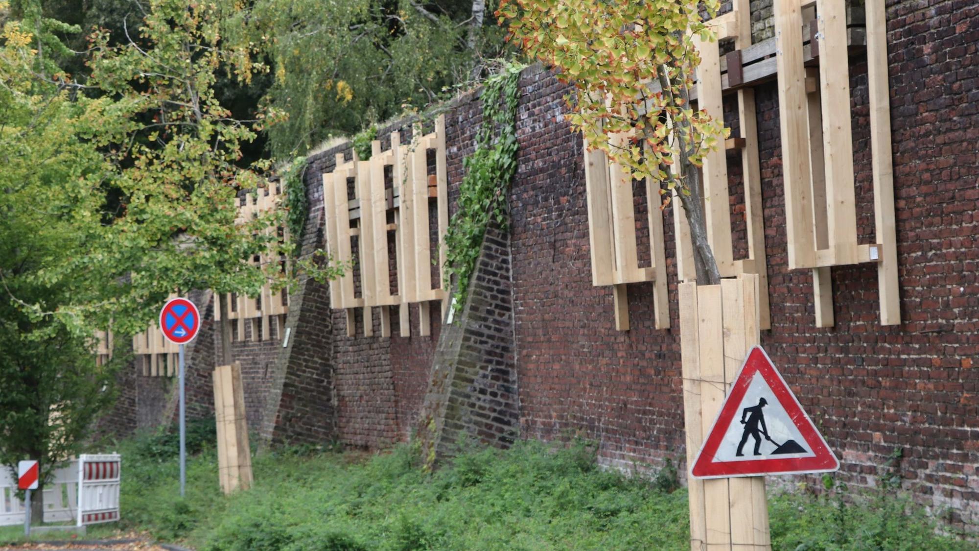 An der Mauer sind Gestelle aus Holz befestigt, sie sichern die Mauer ab.