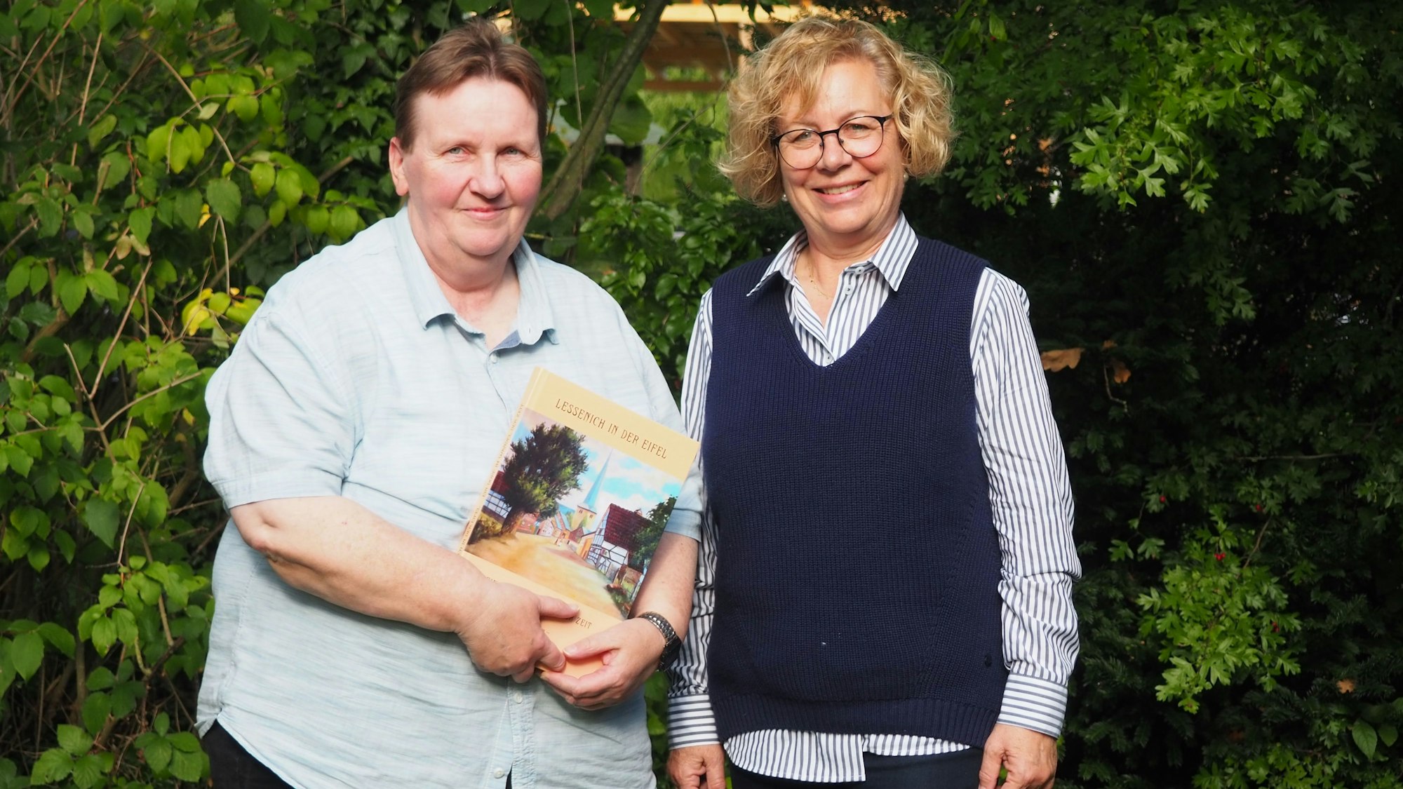 Elisabeth Geusen (l.) und Bärbel Geusen stehen in einem Garten, Elisabeth Geusen hält das Buch in den Händen.