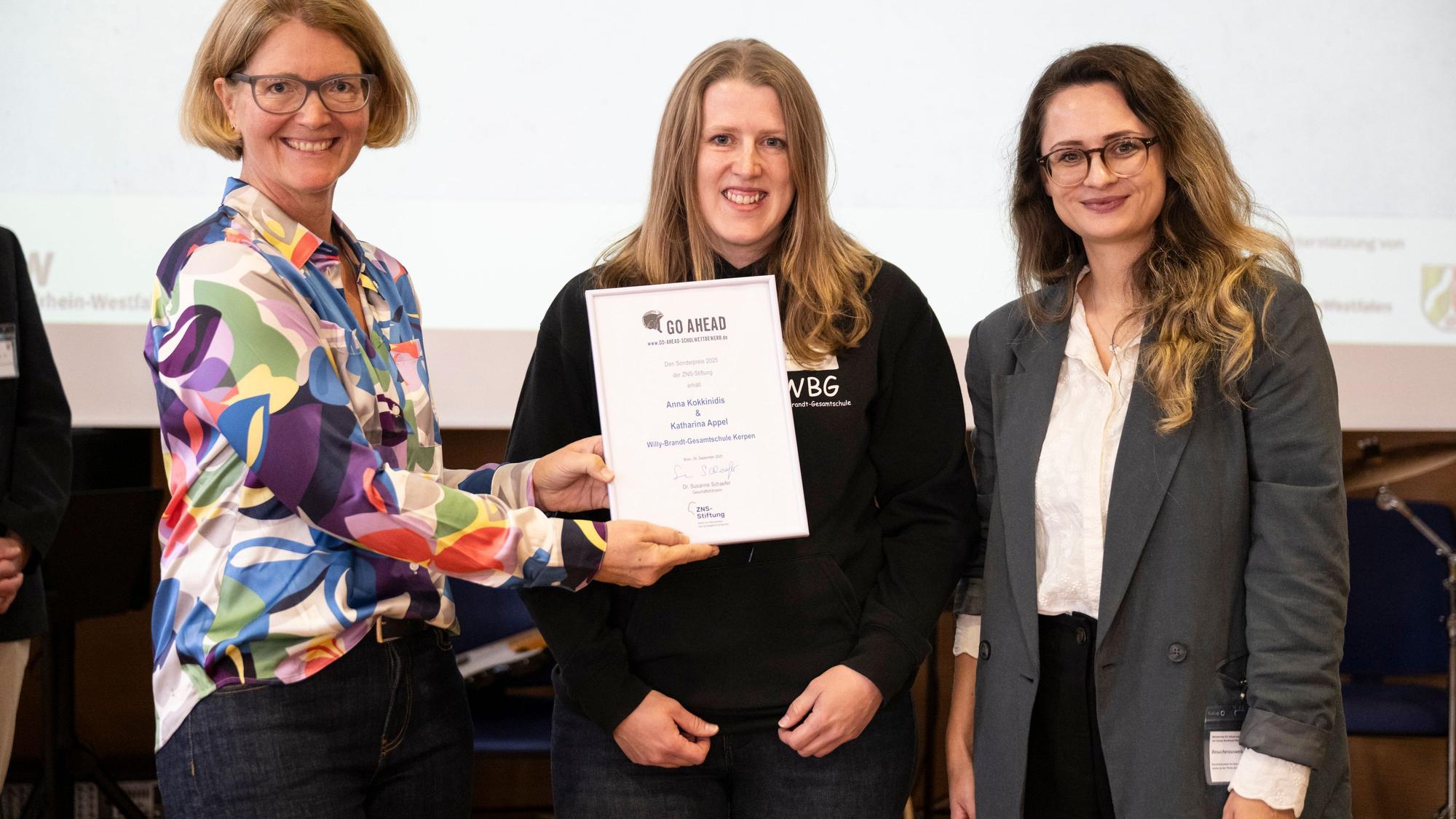 Das Foto zeigt drei Frauen bei der Übergabe einer Urkunde.