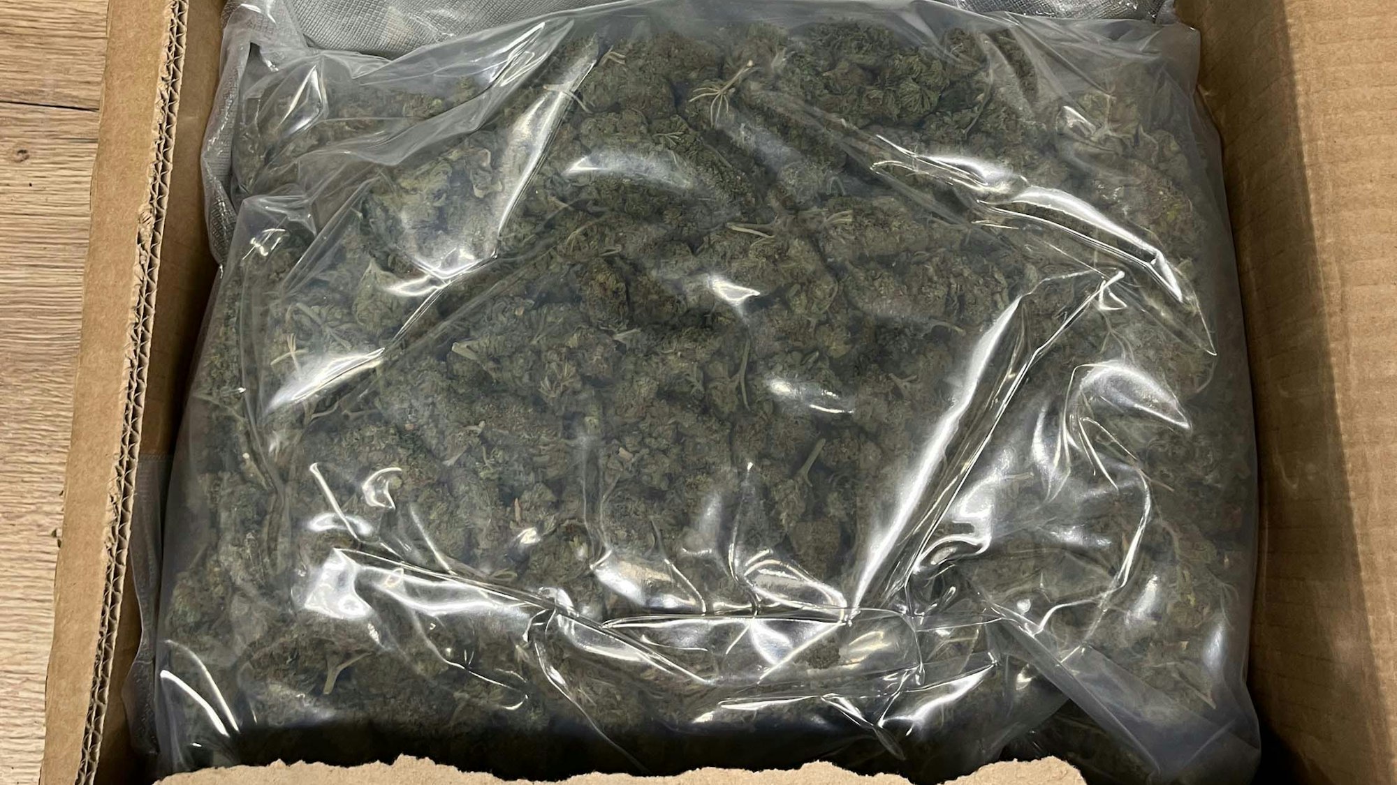 Das Bild zeigt eine große Tüte mit Marihuana in einem Karton.