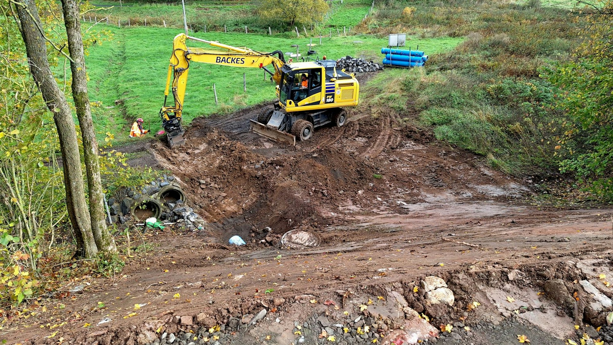 Ein gelber Bagger steht an einer Baustelle an einer Wiese.