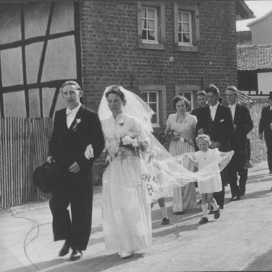 Das Bild zeigt eine Hochzeitsgesellschaft, die eine Dorfstraße entlanggeht.