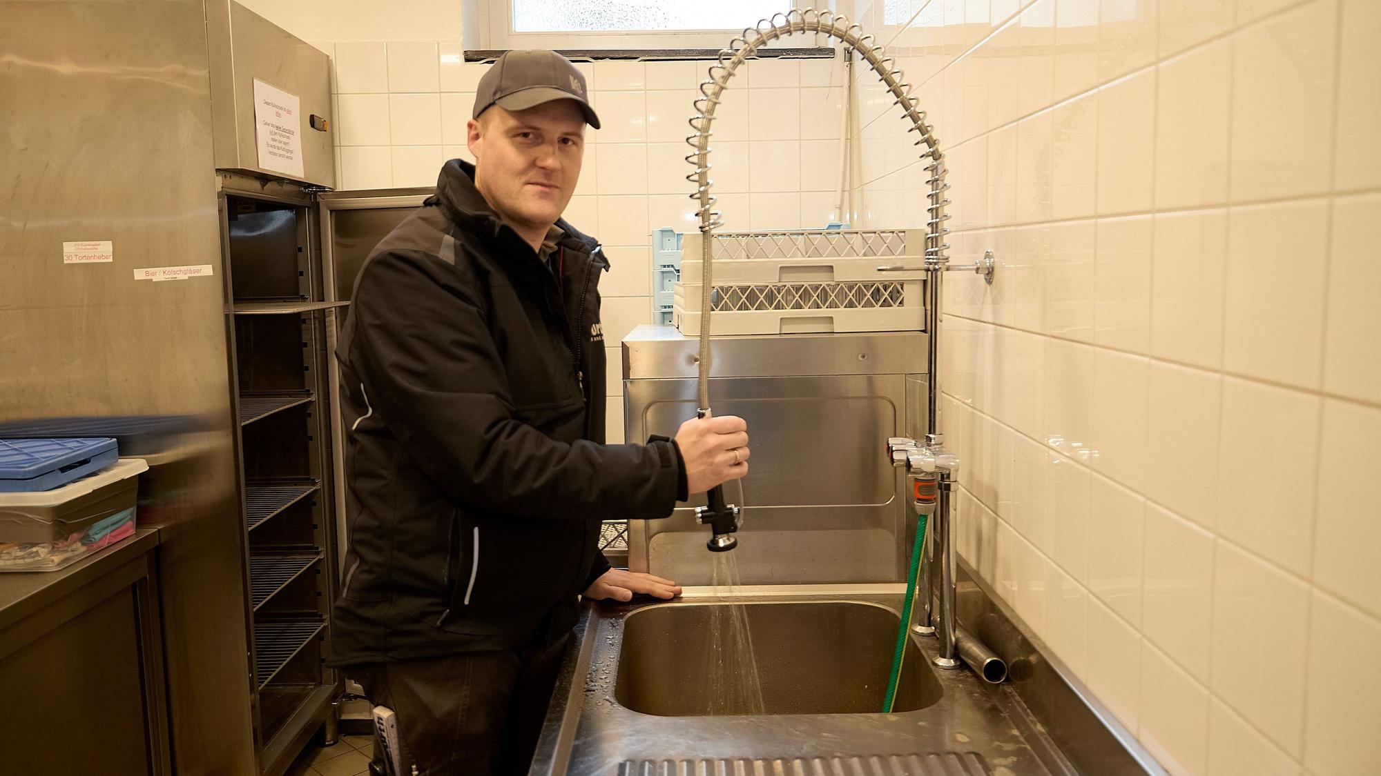 Simon Jung steht in der Spülküche des Dorfsaales in Nettersheim-Tondorf: Aus einem Hahn läuft Wasser in ein Spülbecken.