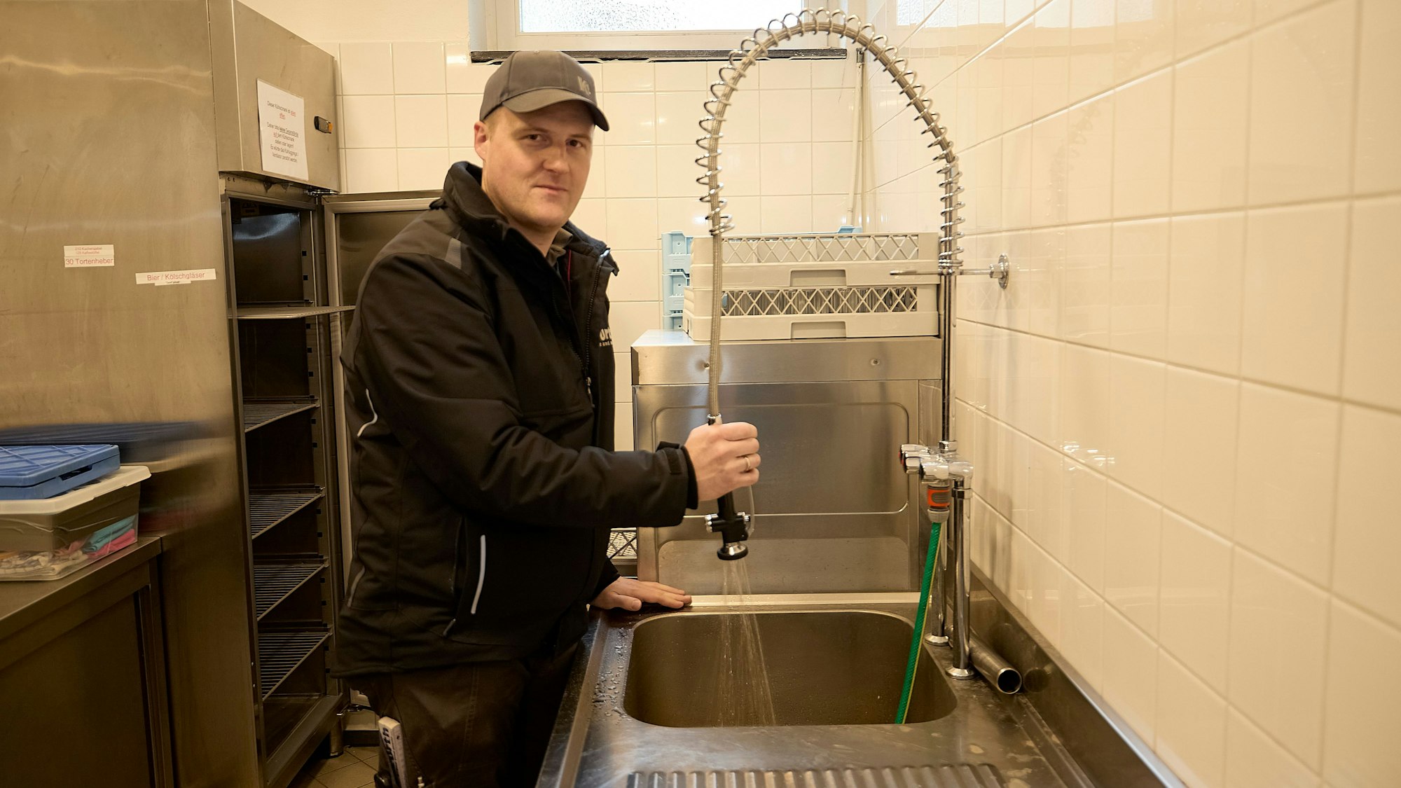 Simon Jung steht in der Spülküche des Dorfsaales in Nettersheim-Tondorf: Aus einem Hahn läuft Wasser in ein Spülbecken.