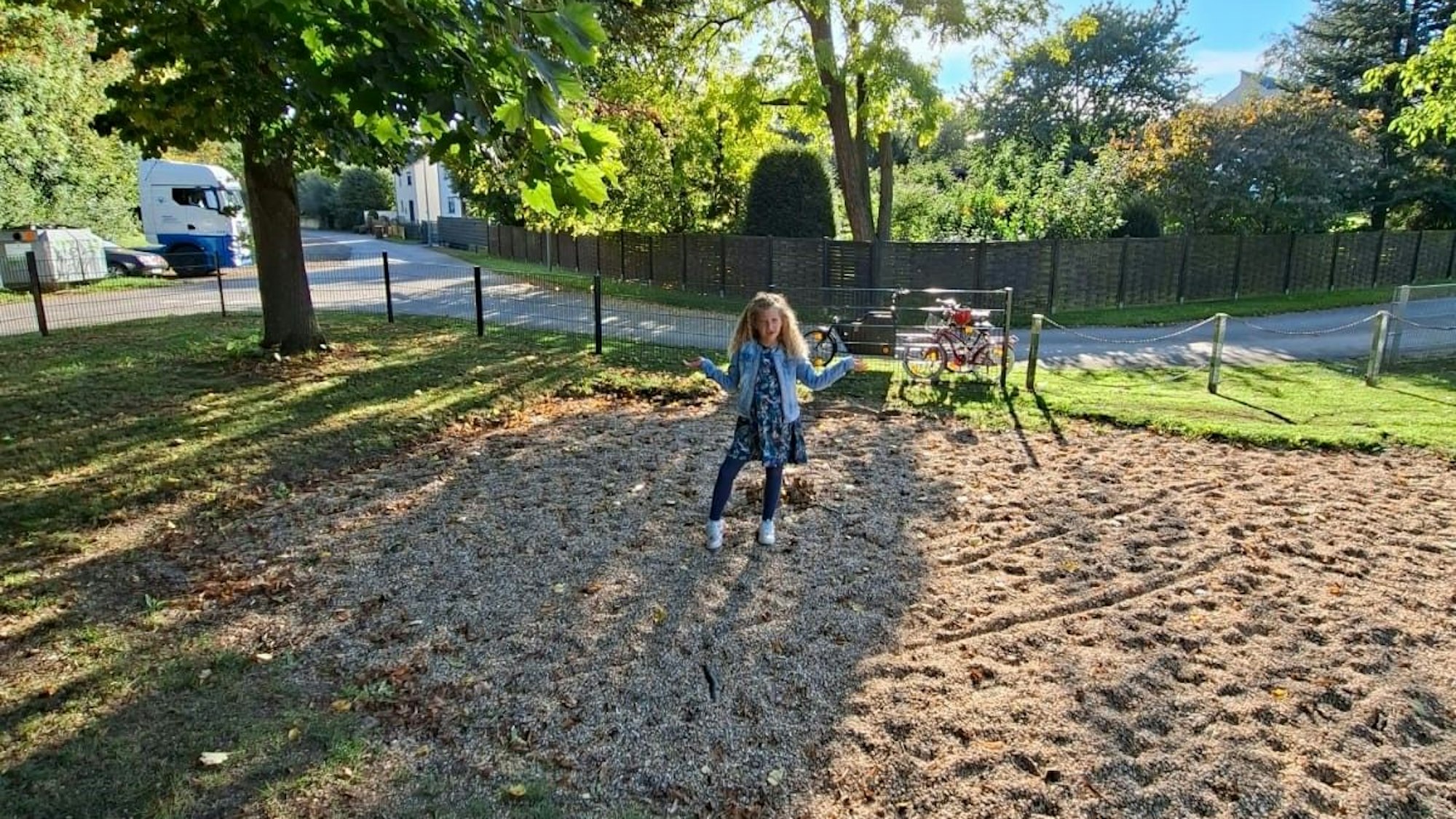 Ein Mädchen steht auf der leeren Kiesfläche des Kessenicher Spielplatzes und hebt fragend die Arme.