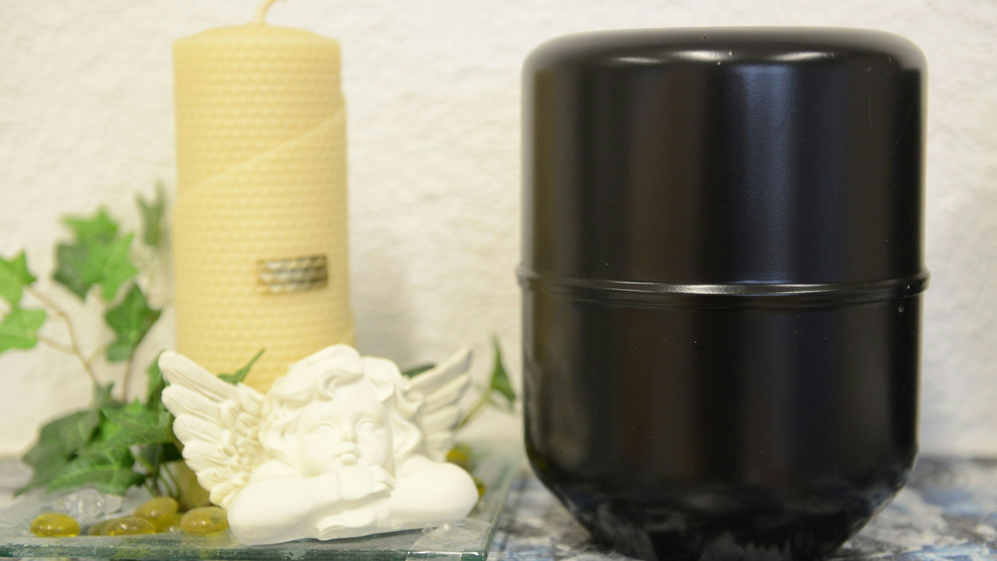 Eine Urne mit der Asche eines Verstorbenen steht bei einem Bestatter neben einer Kerze und einer Engelsfigur.