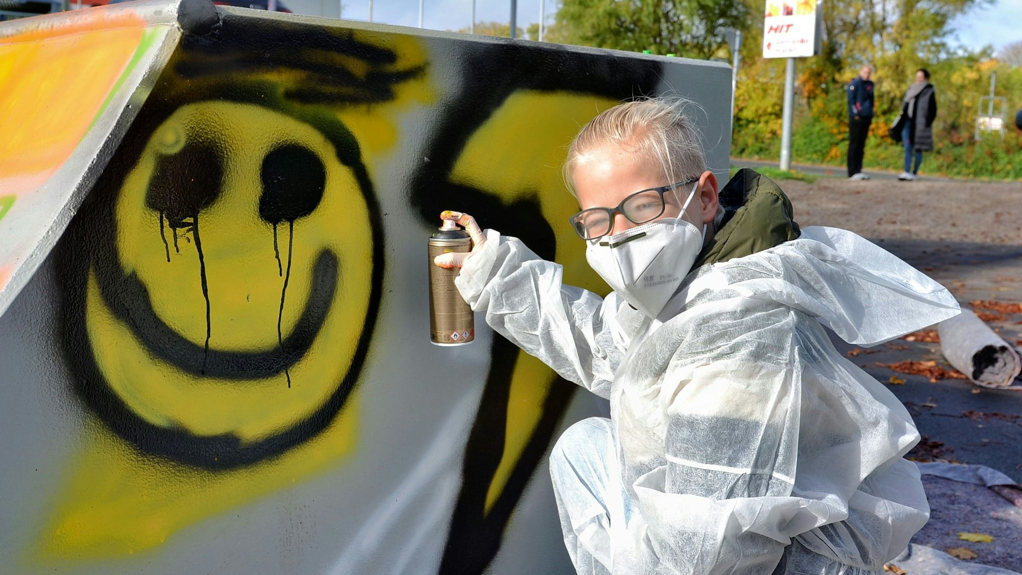 Johann kniet vor der Skateanlage, hält eine Farbspraydose in der Hand. Auf der Anlage ist ein Smiley zu erkennen.