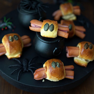 Für die Würstchenspinnen werden die an den Enden eingeschnittenen Wienerstückchen mit Teigstreifen umwickelt. Darauf drückt man je zwei Kürbiskerne als Augen und schiebt das Ganze in den Backofen.