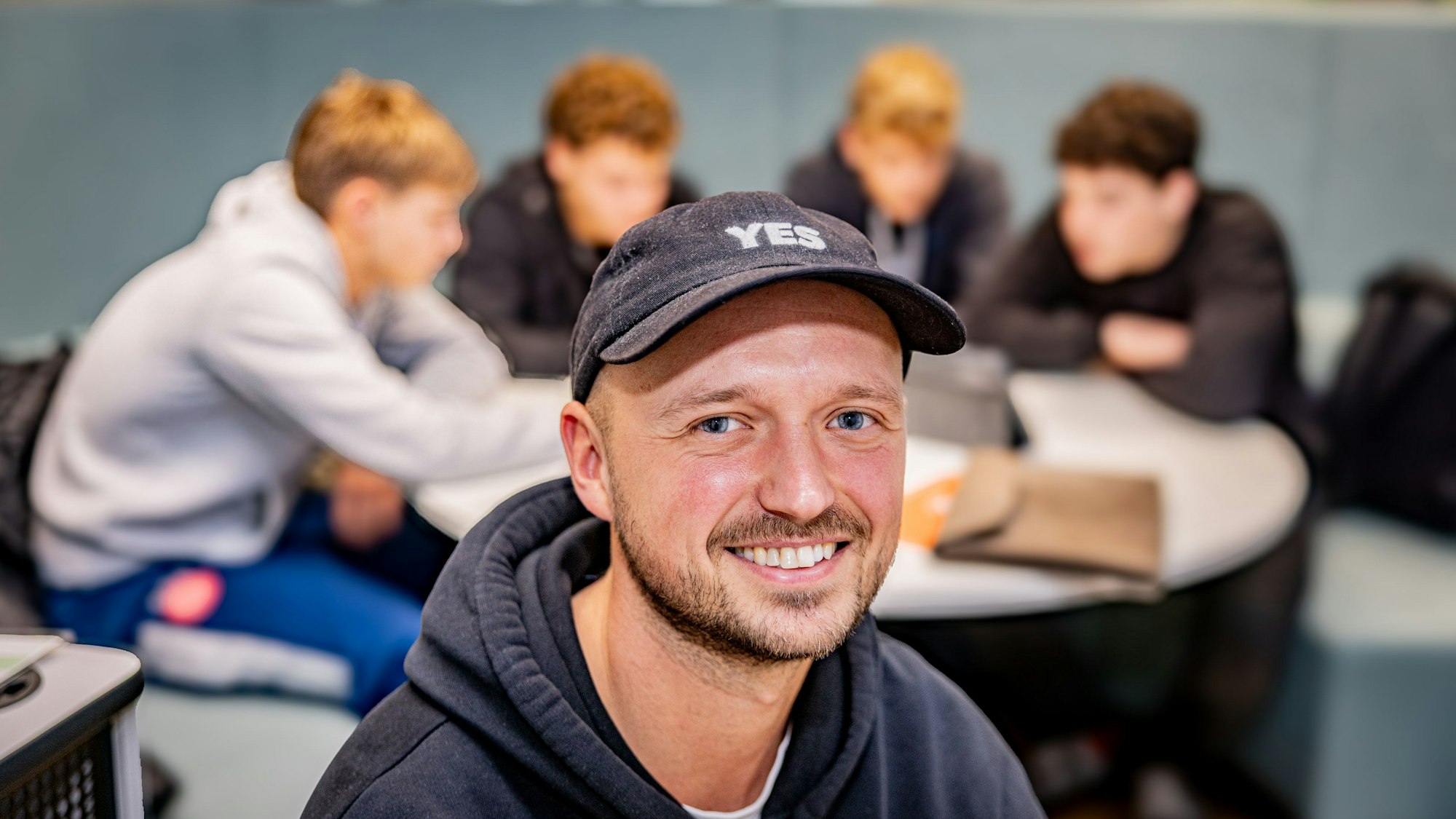 Ein junger Lehrer und einige Schüler im Hintergrund.
