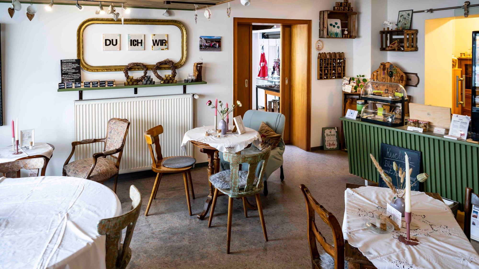 Im Café Dreifachwerk stehen einige Tische mit unterschiedlichen Stühlen. Rechts ist eine grüne Theke.