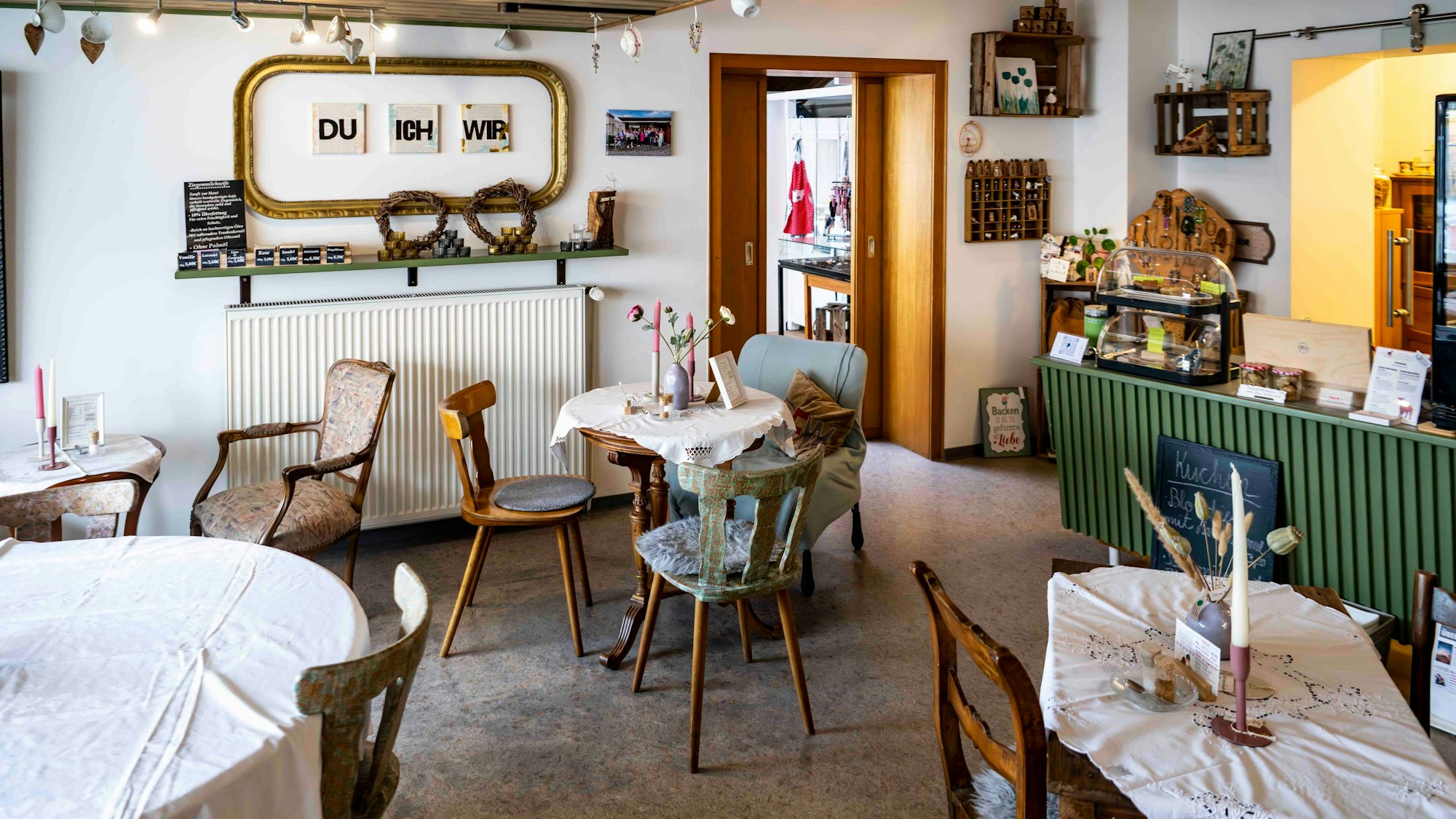 Im Café Dreifachwerk stehen einige Tische mit unterschiedlichen Stühlen. Rechts ist eine grüne Theke.